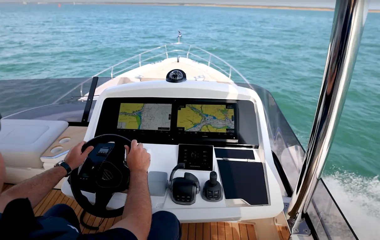 A person steering a boat, using navigation screens displaying maps, with water visible in the background.